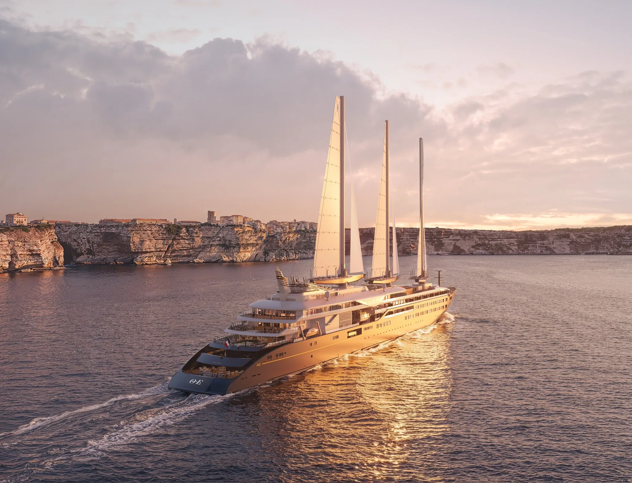 Three-masted sailing yacht Corinthian gliding past Bonifacio limestone cliffs at golden sunset