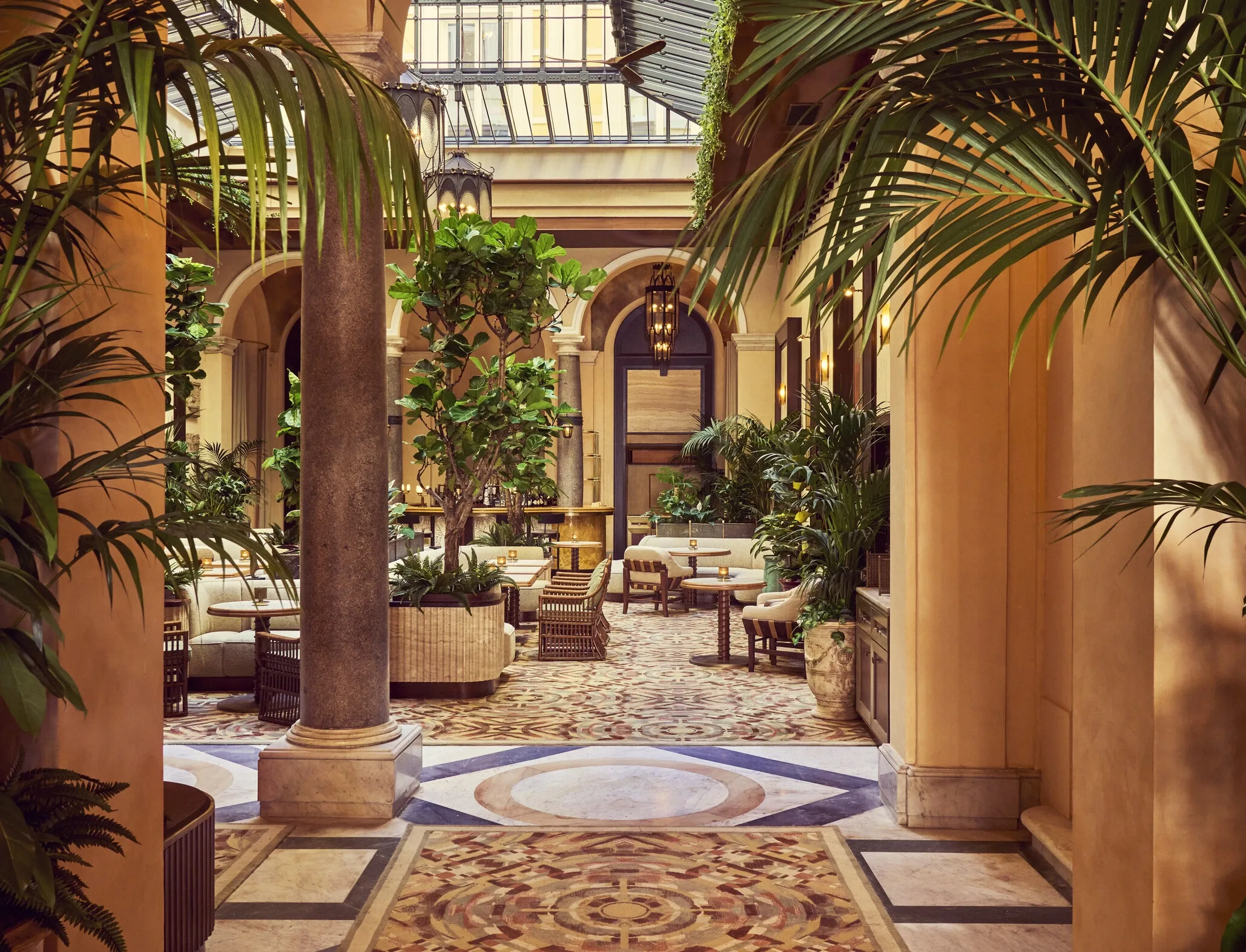 Orient Express hotel entrance showing marble column and palm-filled atrium with patterned mosaic floor and glass roof 