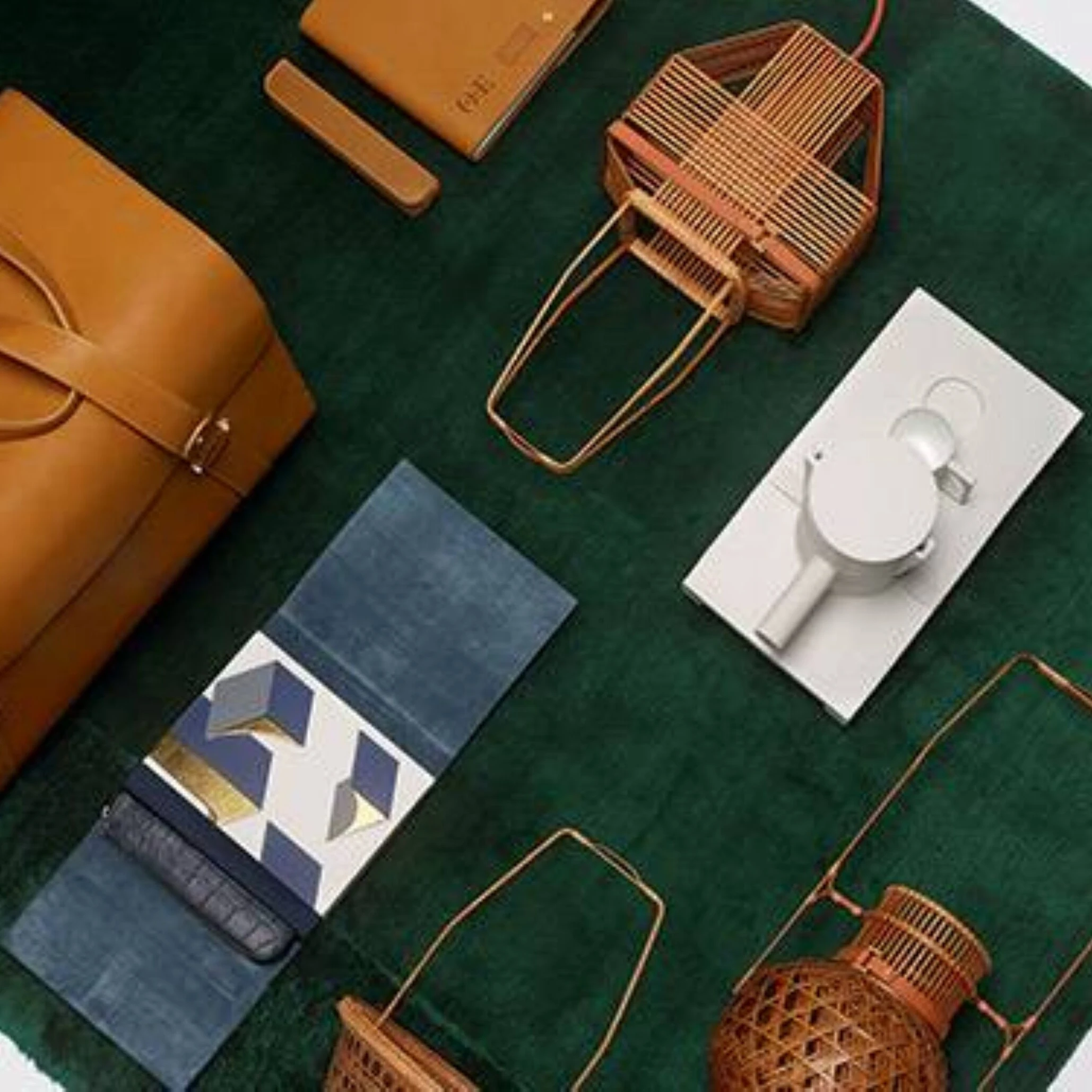 Orient Express leather duffel and curated travel accessories arranged on deep green velvet backdrop 