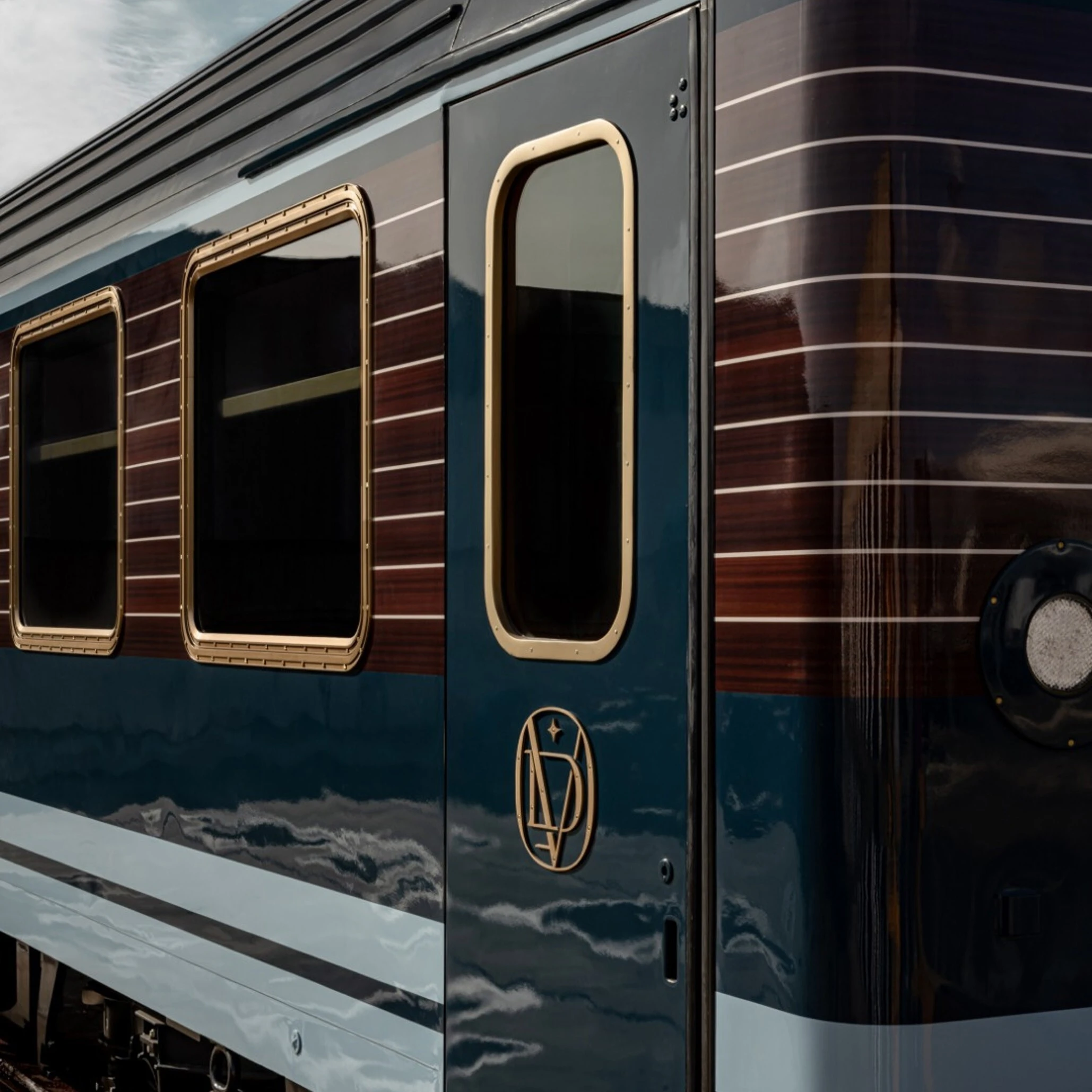 Le Grand Tour carriage with polished navy body and brass-framed windows reflecting clouds on the Orient Express 