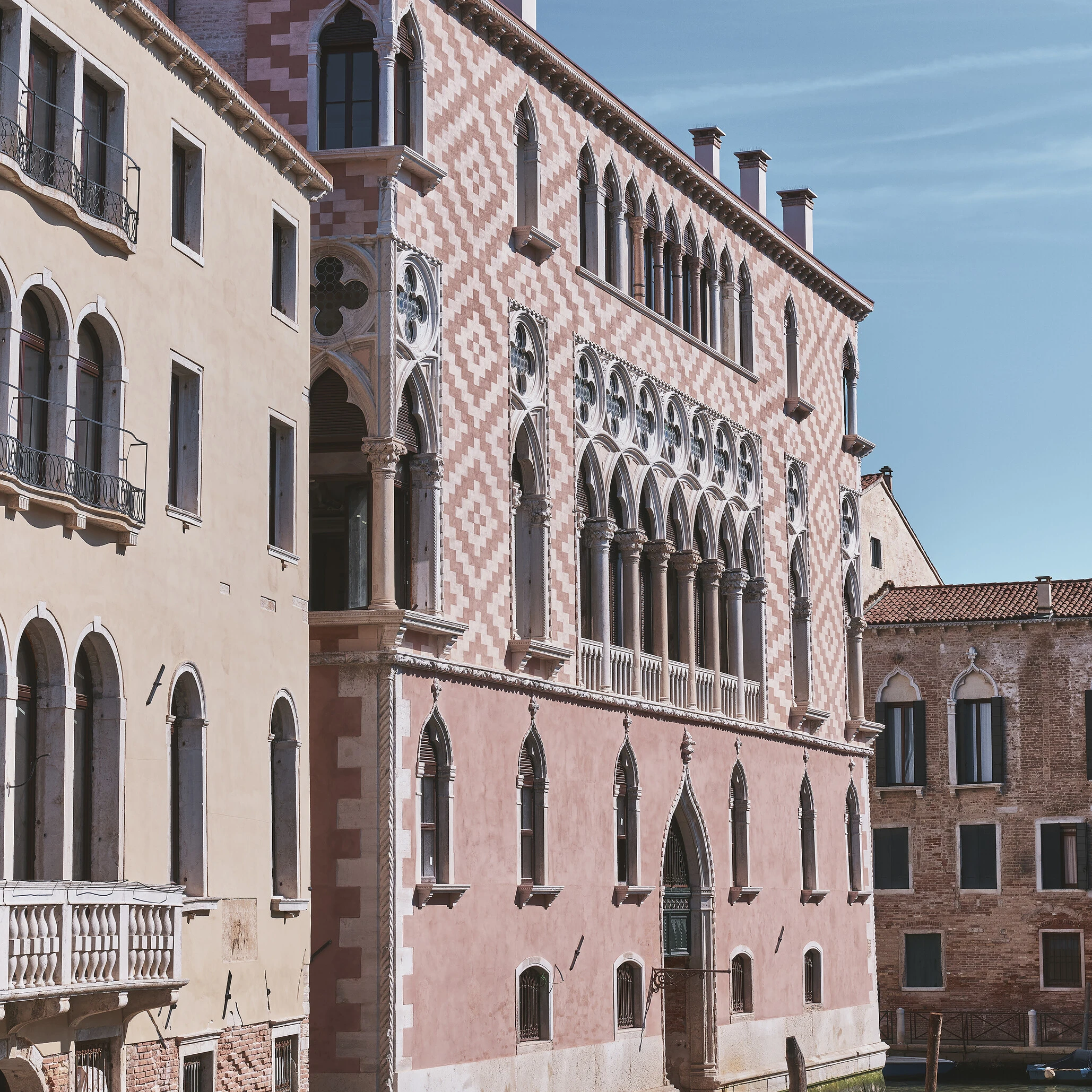 Orient Express façade showing ornate Venetian Gothic arches and pink chequered marble on a canal-side palazzo under blue sky 