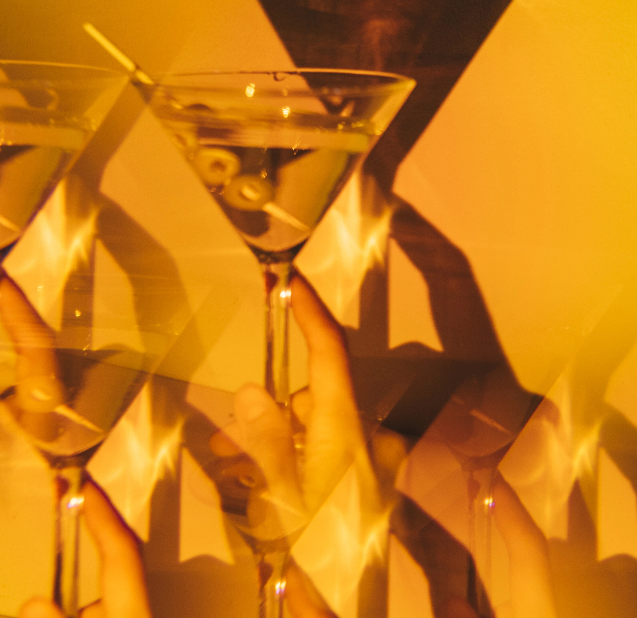 Gorda martini glass with olives held in hand, layered reflections in warm amber gala bar lighting 