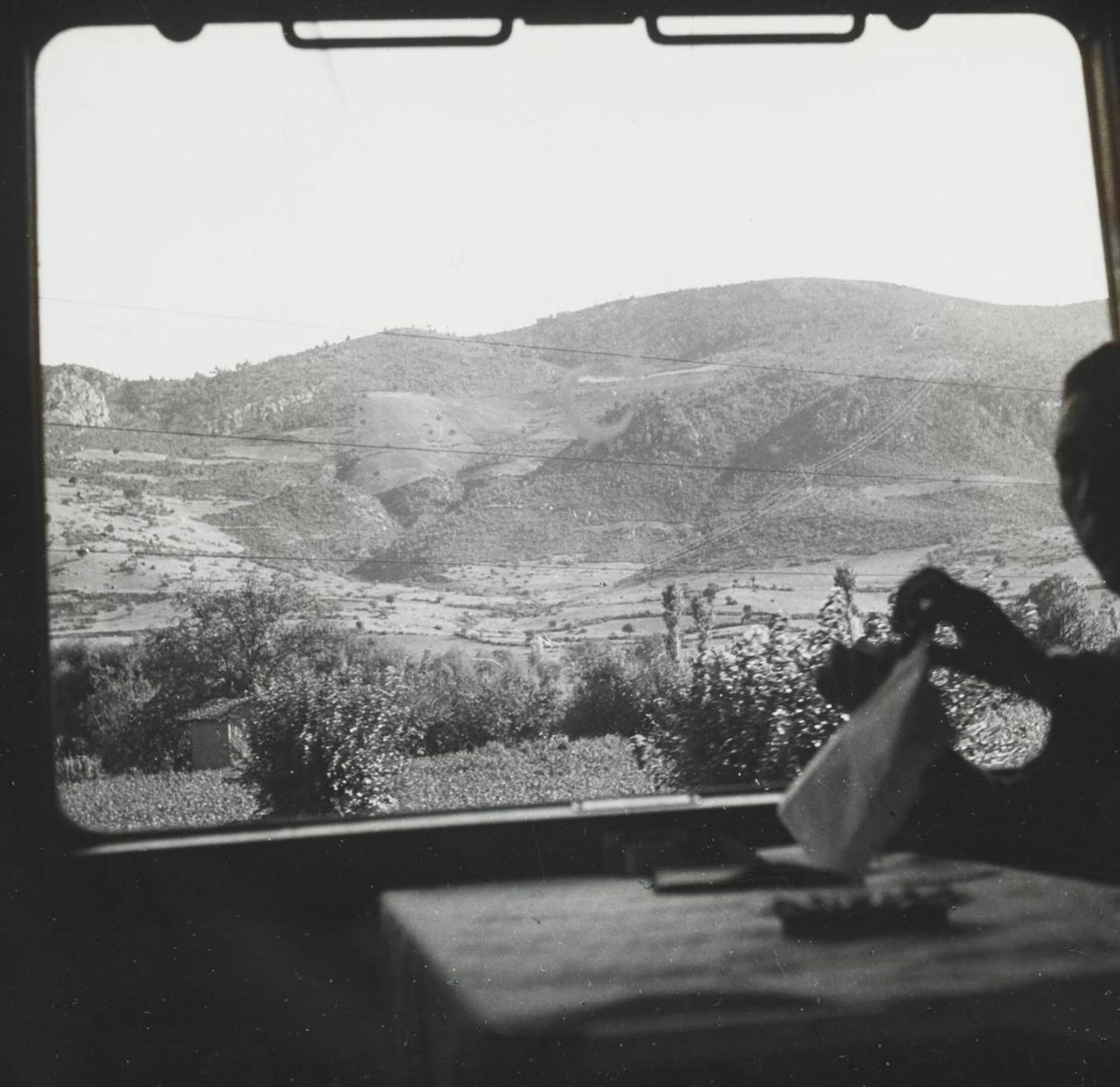 Orient Express passenger unwrapping a napkin at a table, view through carriage window of rolling hills and fields 